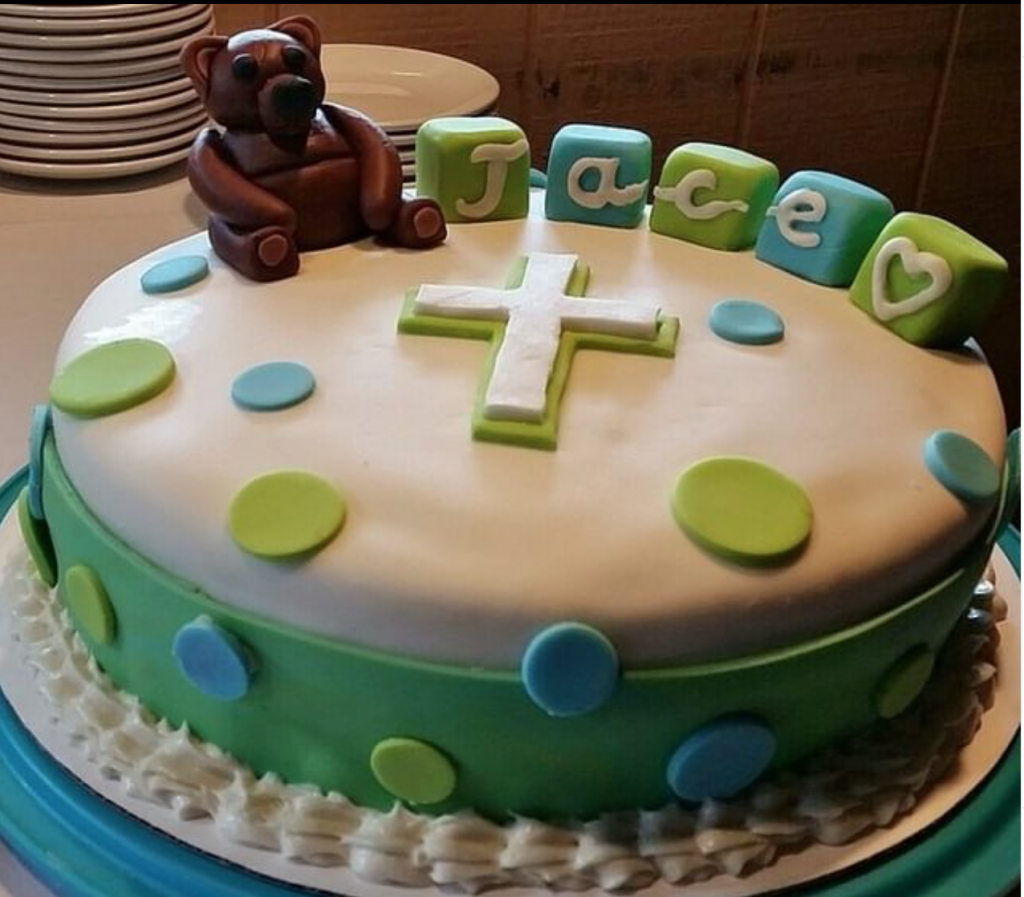 Round cake, with green and blue polka dots all over.  The top has a white and green Christian cross, cubes with letters on them, and a brown bear.